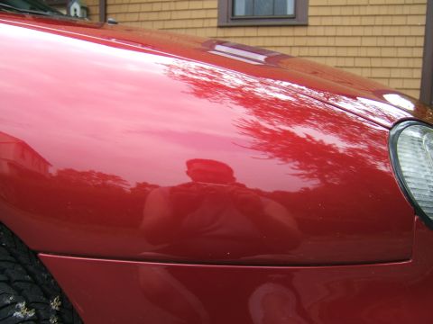 1998 Ford Taurus - Reflections of trees and a person are visible on the polished surface of a red car's fender.