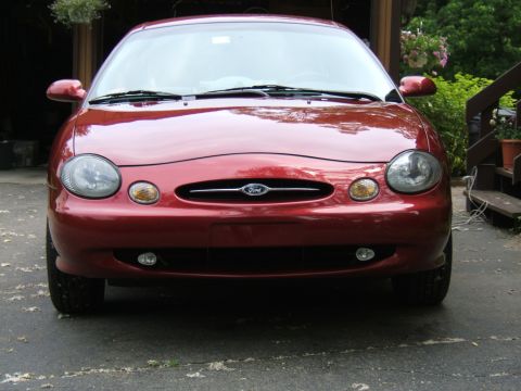 1998 Ford Taurus - The front of a red 1998 Ford Taurus is shown, parked in front of a garage.