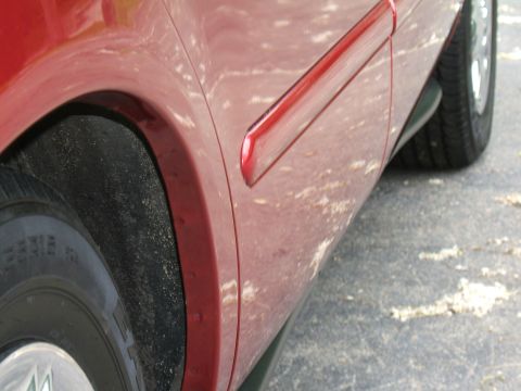 1998 Ford Taurus - Close-up view of a red car's side panel and wheel, showing a red trim piece.