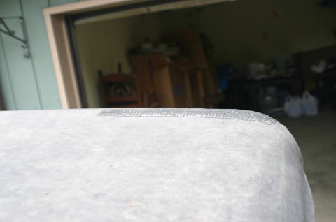 2003 Jeep TJ - A gray soft top with a taped seam is visible in the foreground, with a garage interior blurred in the background.