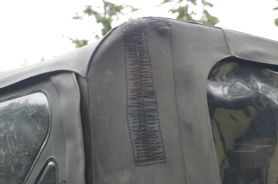 Close-up of a black Jeep soft top corner with visible stitching and a clear plastic window