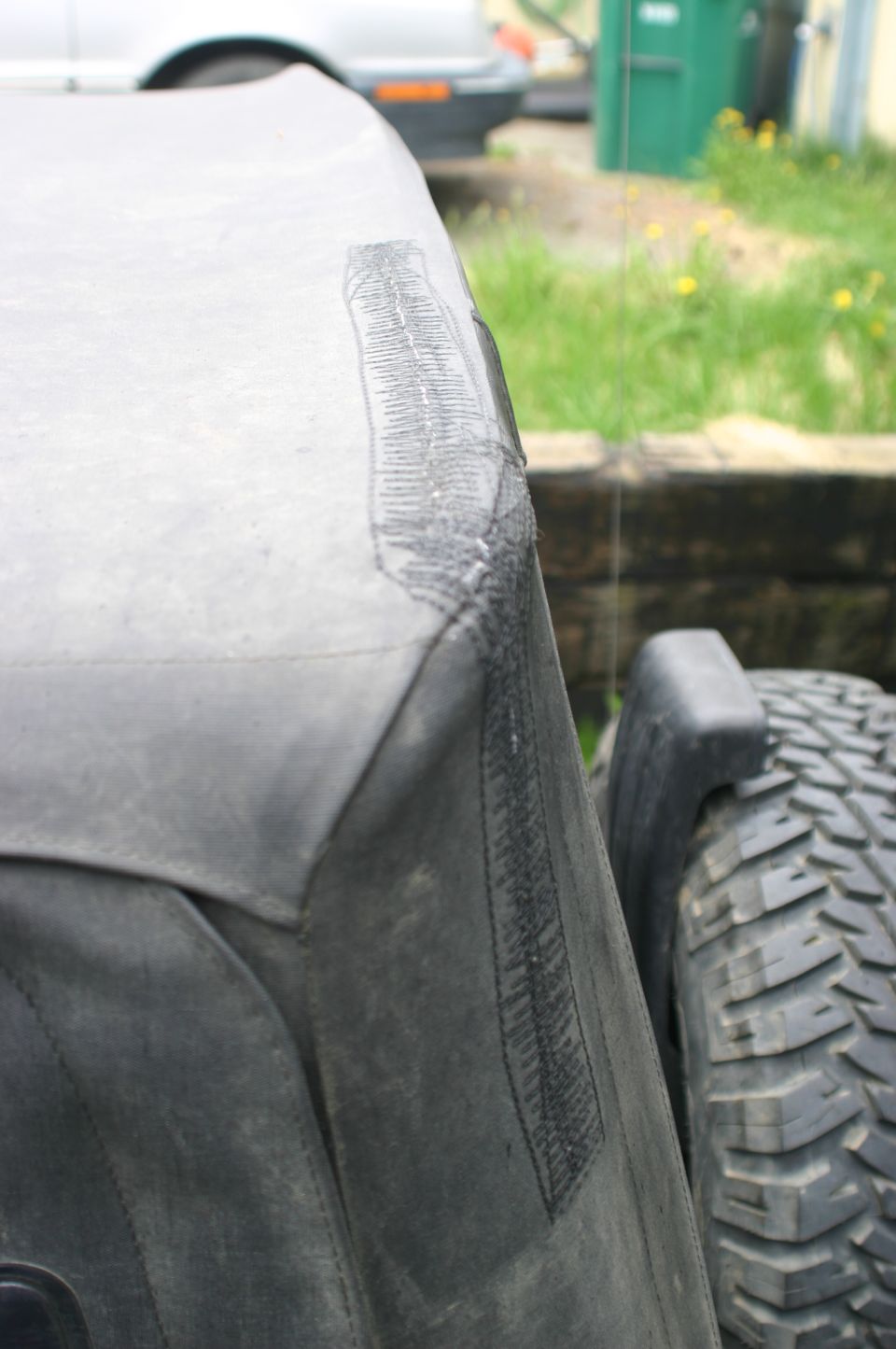Close-up of a patched rip on a Jeep soft top, with a tire visible to the right