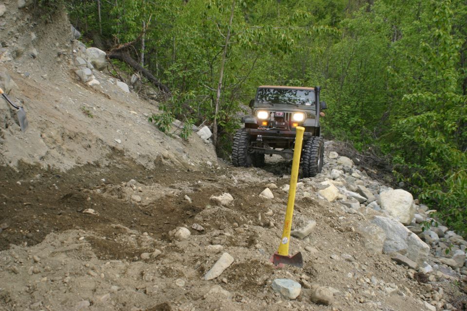 Green Jeep Wrangler on a rocky, dirt trail with trees in the background