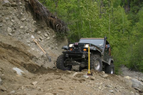 2003 Jeep TJ - A Jeep Wrangler navigates a challenging off-road trail, with shovels visible on the embankment.
