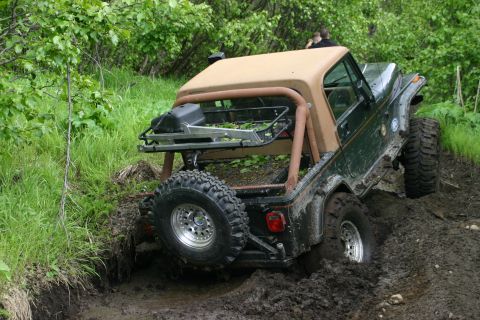 2003 Jeep TJ - A green Jeep Wrangler with a tan soft top navigates a muddy trail, getting stuck in the mire.