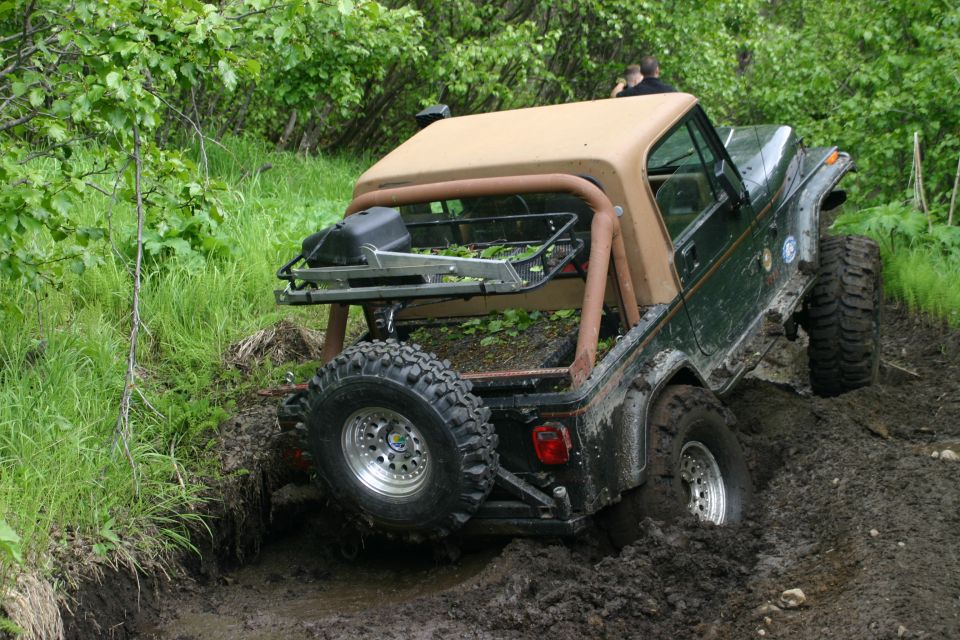 Green Jeep Wrangler with tan soft top stuck in mud, rear view