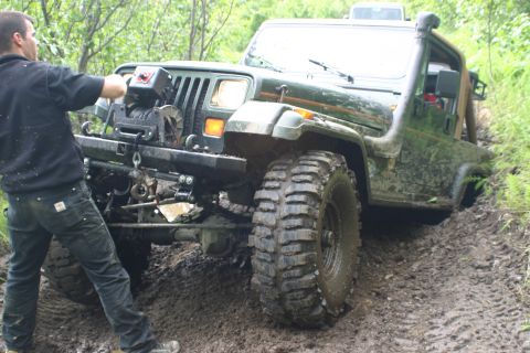 2003 Jeep TJ - A person operates a winch on a green Jeep Wrangler TJ stuck in thick mud on a trail.