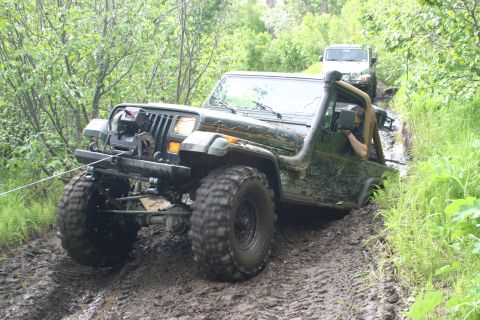 2003 Jeep TJ - A Jeep navigates a challenging muddy off-road course with another vehicle following.