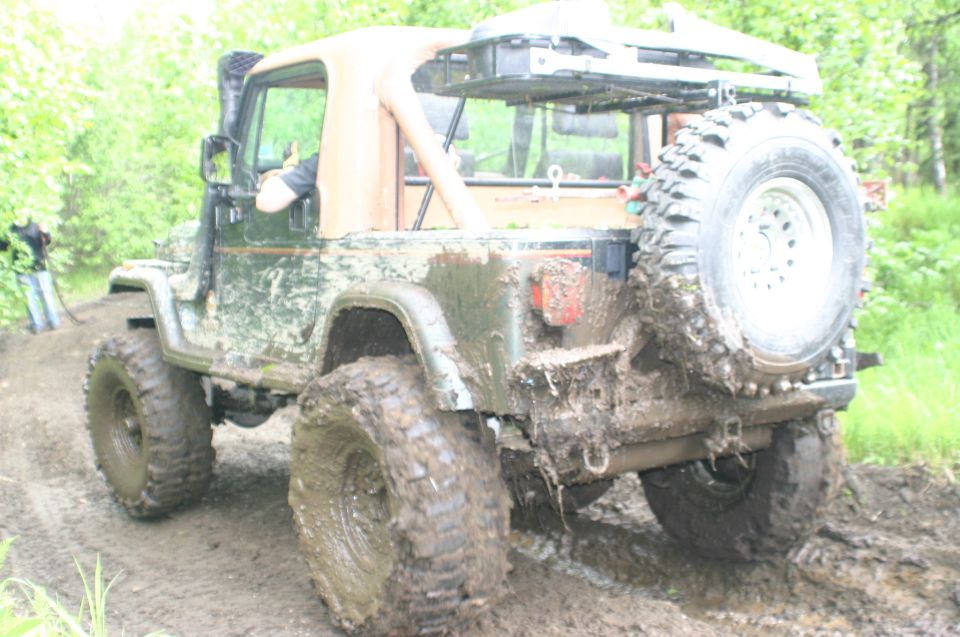 Mud-covered Jeep Wrangler with a spare tire on the back, driving through a muddy trail