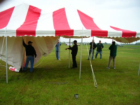2003 Jeep TJ - Several individuals are working together to erect a large tent with red and white stripes.