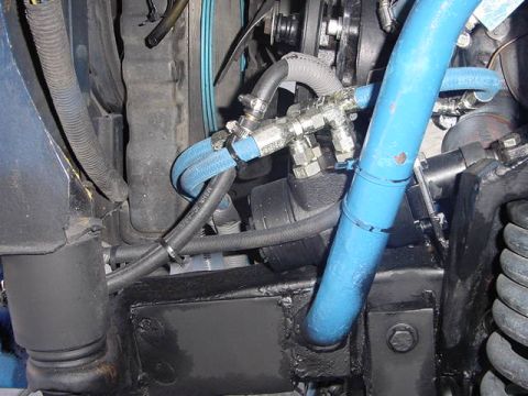 1971 Ford Bronco - Close-up view of engine components, including blue hoses and various metal fittings.