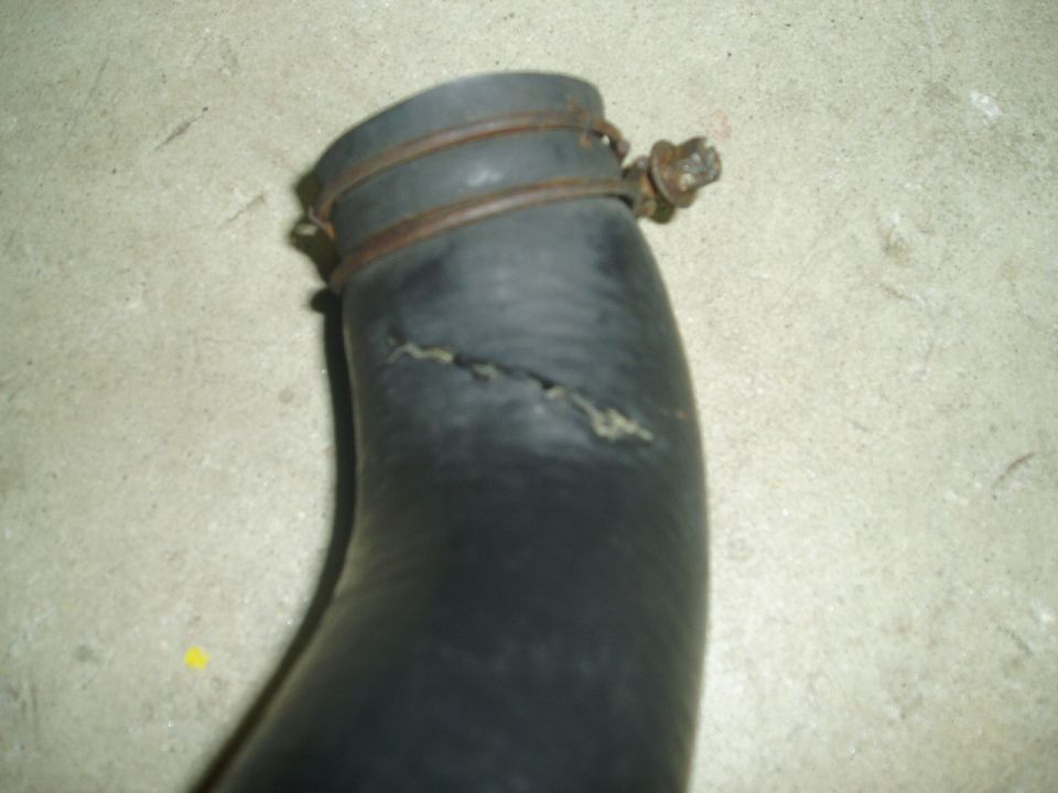 Close-up of a black rubber radiator or coolant hose with a longitudinal crack on concrete