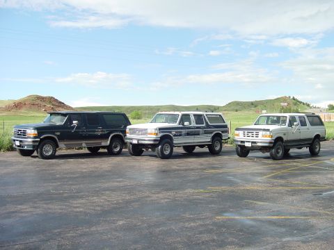 1994 Ford C-350 (Centurion Conversions) - Three Ford C-350 Centurion conversion SUVs are lined up in a parking lot under a partly cloudy sky.