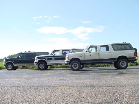 1994 Ford C-350 (Centurion Conversions) - Three extended cab pickup trucks are lined up on the side of a road under a partly cloudy sky.