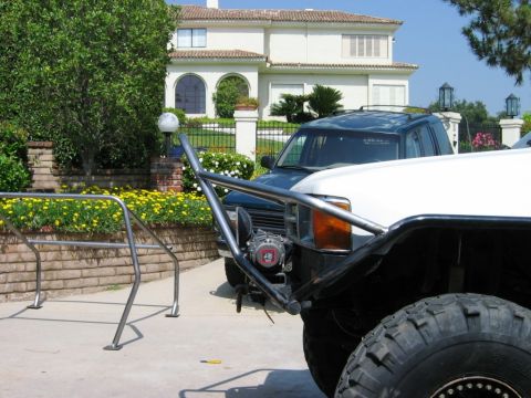 1985 Ford Bronco - A white off-road truck with a custom bumper and large tires is parked in front of a house.