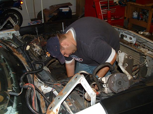 Man bent over working on a car engine bay with many wires visible
