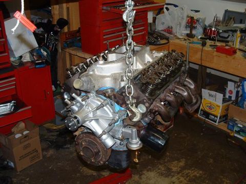 1985 Ford Crown Victoria LTD - An engine is suspended by a chain hoist in a workshop, surrounded by tools and storage cabinets.