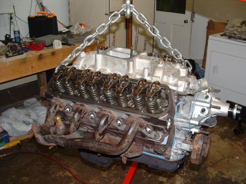 1985 Ford Crown Victoria LTD - An engine is suspended by chains, ready for installation or removal, with visible valve train components and exhaust headers.