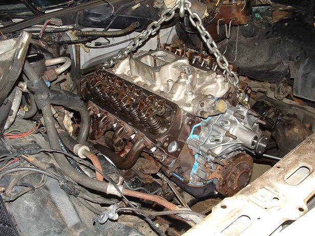 Engine being lifted out of a vehicle's engine bay by a chain hoist. Wires and hoses are visible