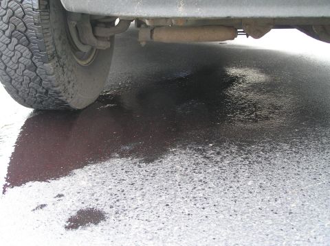 2000 Ford Excursion - Dark fluid is leaking onto the asphalt from under the vehicle's chassis.