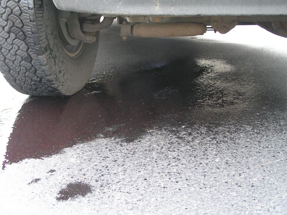 Vehicle undercarriage with tire above a dark reddish fluid leak on wet asphalt