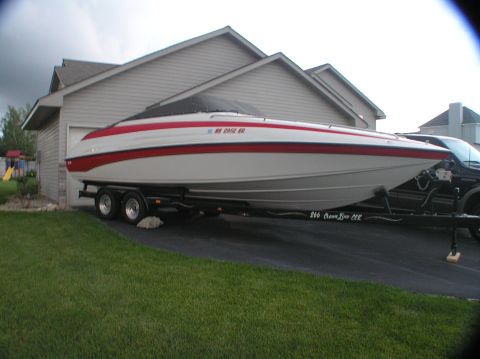 2000 Ford Excursion - A white and red boat with a black cover is parked on a trailer in front of a residential garage.