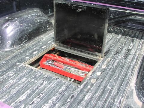 1979 Ford Bronco - A black storage compartment in a truck bed contains a red case filled with various wrenches.