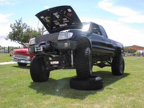 1979 Ford Bronco - A heavily modified black pickup truck is parked on a grassy field next to a vintage red truck.