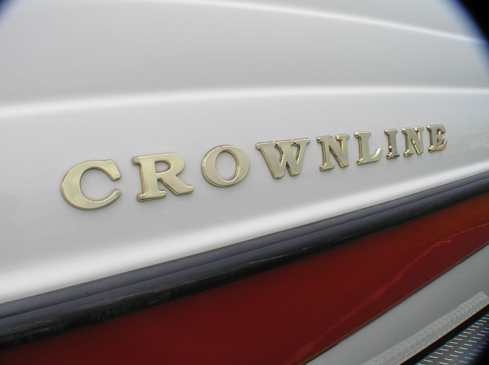 Gold CROWNLINE emblem on white boat hull with maroon stripe