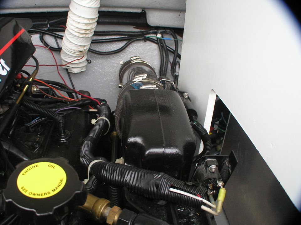 Marine engine bay with black engine, yellow oil cap, hoses and wiring in a boat hull.