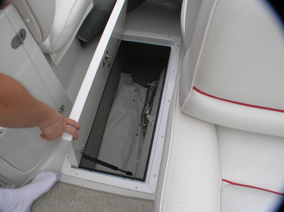 Open in-floor storage compartment on a boat with gray cover inside and white seats nearby