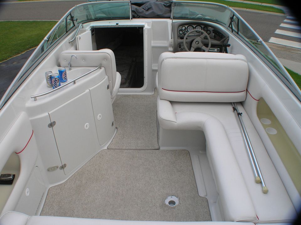 White boat cockpit interior with helm, wheel, gauges, bench seats, and gray carpet