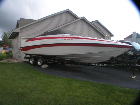 1997 Crownline 266 CCR - A white and red boat on a trailer is parked in front of a residential garage, partially obscured by a black truck.