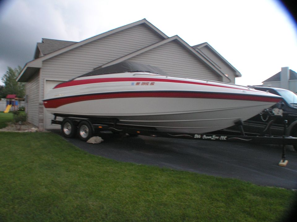 White and red powerboat with cover on a dual-axle trailer in a driveway