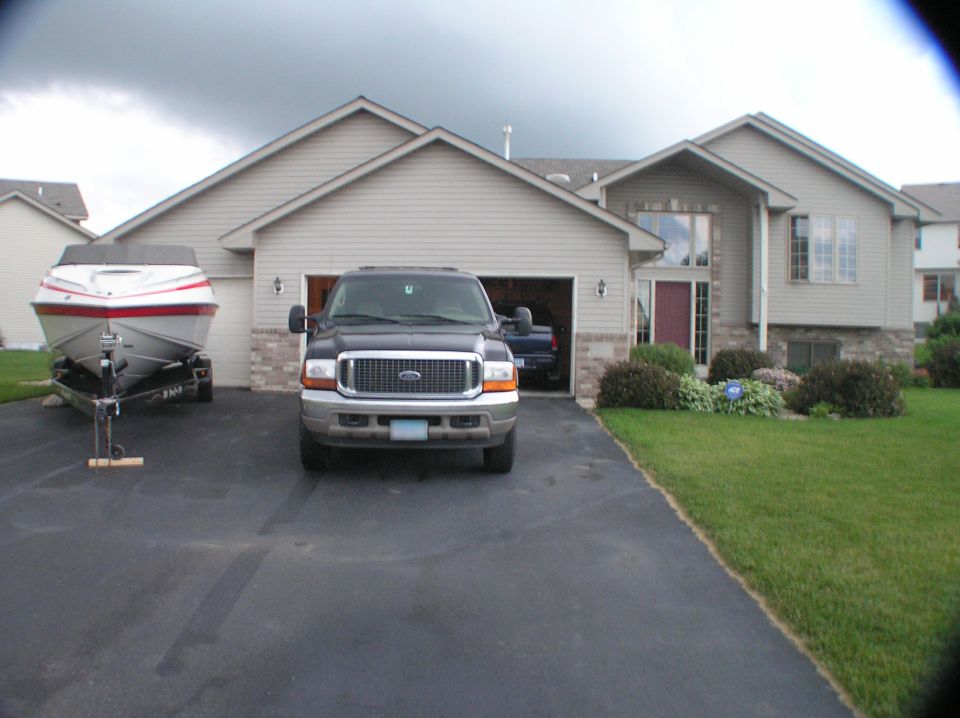 White and red boat on trailer beside dark gray Ford SUV in a home driveway