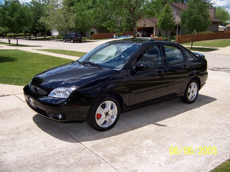 Black 2005 Ford Focus sedan parked on a concrete driveway in front of a house