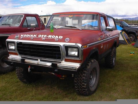 1978 Ford Bronco - A red 1978 Ford Bronco is parked on grass with tents and other vehicles in the background.