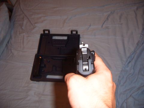1988 Ford Bronco - A hand grips a pistol, aiming it forward with a gun case open behind it on a rumpled bed.