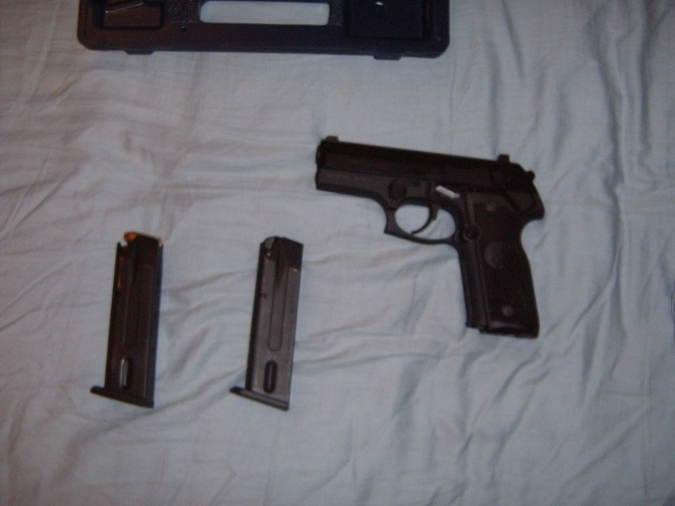 Black pistol with two spare magazines and a black case on a white cloth surface