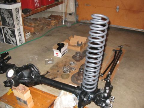 1995 Ford Bronco - Vehicle axle and suspension parts are disassembled and arranged on the floor, likely for repair or modification.