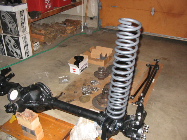 Rebuilt black front axle with tall silver coil spring on garage floor