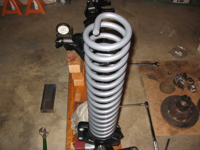 Gray coil spring on black axle housing surrounded by tools in a garage.