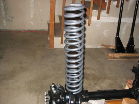 1995 Ford Bronco - A gray coil spring is mounted on a black axle assembly, likely for an off-road vehicle modification.