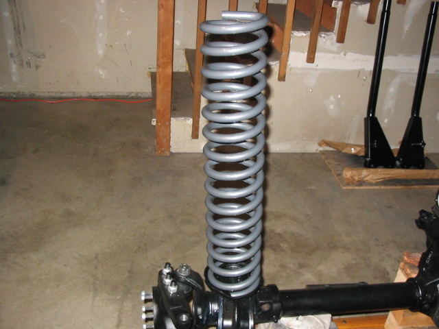 Gray coil spring over black suspension axle component on garage floor