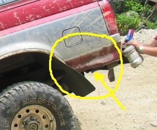 1995 Ford Bronco - Close-up of the rear quarter of a maroon truck with a dent and crease circled in yellow marker and an arrow drawn to it; a mud tire and dir…
