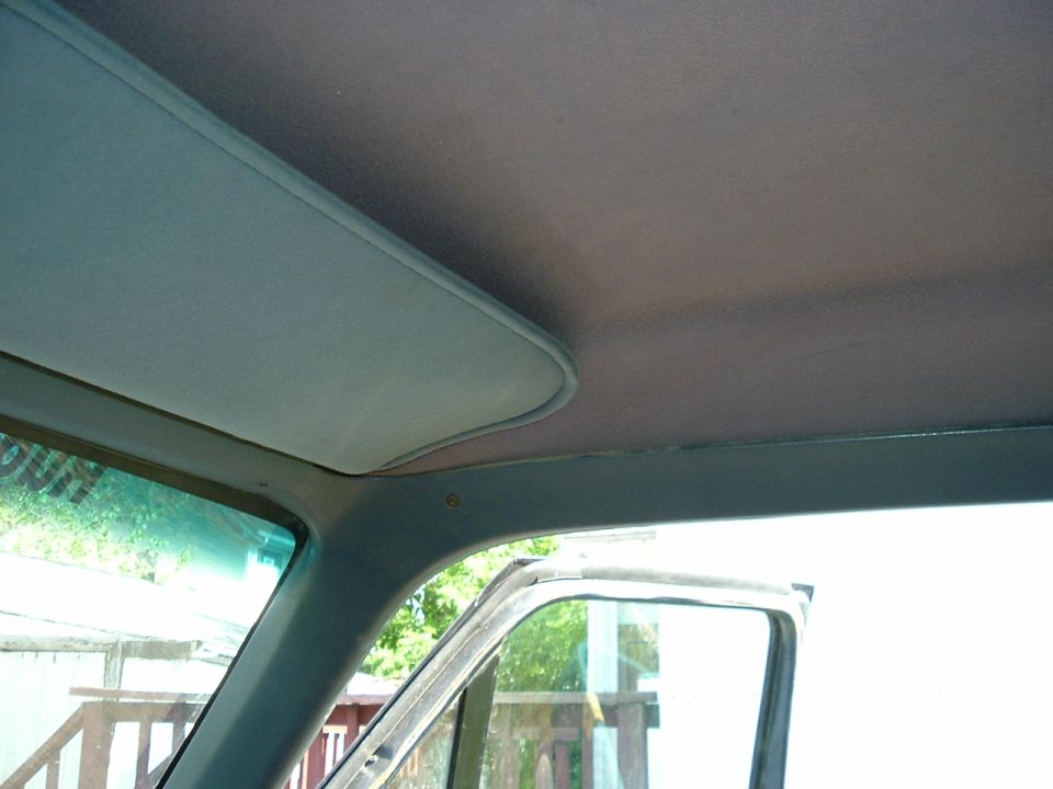 Interior view of a car's headliner and sun visor, with a partial view of the open door and window