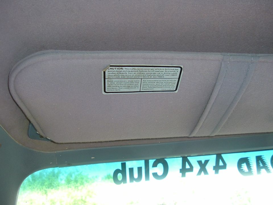 Interior view of a vehicle's sun visor with a caution label. Text on visor is partially visible