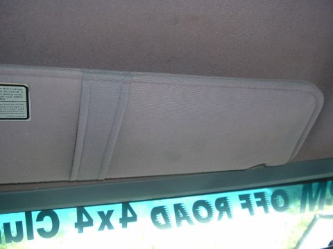 1989 Ford Bronco - The interior of a vehicle shows a sun visor and a reflection of off-road club text on the windshield.