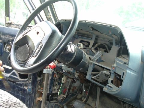 1989 Ford Bronco - The dashboard of a vehicle is partially disassembled, revealing the steering column and wiring harness.