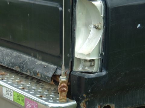 1989 Ford Bronco - The taillight assembly is broken, showing internal components and a light bulb. Rust is present on the vehicle's lower body and bumper.